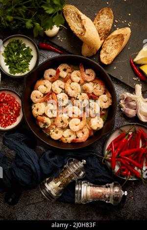 Gebratene Baby Shrimps auf Eisenpfanne und frischen Kräutern und Zutaten serviert. Draufsicht, flach liegend Stockfoto