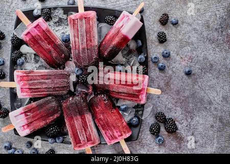 Hausgemachte frische gefrorene Heidelbeere und Brombeerpopsicles auf schwarzem Teller mit Eis auf Stein sitzen Stockfoto