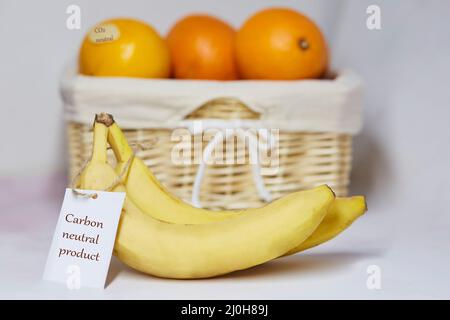 Kohlenstoffneutrales Produktetikett auf Bananen. CO2-Kennzeichnung. Korb mit Orangen auf dem Hintergrund. Netto kohlenstofffrei, emissionsfrei. Bio-Landwirtschaftsprodukte aus Stockfoto