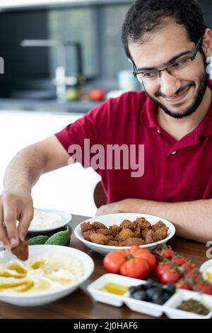 Junger Mann aus dem Nahen Osten sitzt und isst traditionelles Essen Stockfoto