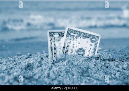 Zwei ein-Dollar-Scheine, die zur Hälfte im Sand an der sandigen Küste aus nächster Nähe vergraben sind. Stockfoto