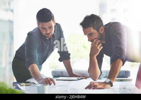 Mit einem Plan zusammenkommen. Aufnahme von zwei jungen Designern, die in einem Büro an Blaupausen arbeiten. Stockfoto