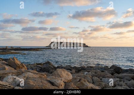 Felsige Küste von Agios Georgios Zypern. Blick auf die Insel Yeronisos. Sonnenuntergang am Hafen von Agios Georgios Pegeias in Paphos, Zypern. T Stockfoto