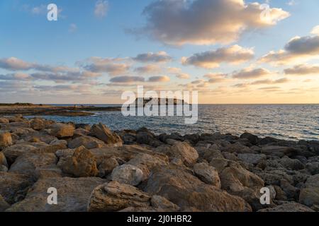 Felsige Küste von Agios Georgios Zypern. Blick auf die Insel Yeronisos. Sonnenuntergang am Hafen von Agios Georgios Pegeias in Paphos, Zypern. T Stockfoto