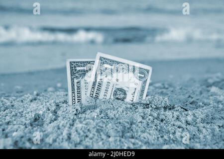 Zwei ein-Dollar-Scheine, die zur Hälfte im Sand an der sandigen Küste aus nächster Nähe vergraben sind. Stockfoto