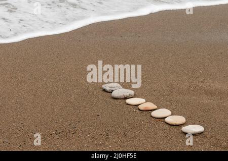 Glatte Strandsteine in einem rohen an einer sandigen Küste und Schaum von Meerwasser. Stockfoto