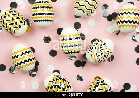 Osterkomposition. Goldene, schwarze Ostereier mit geometrischem Design, Konfetti auf pastellrosa Hintergrund. Flach liegend, Draufsicht. Stockfoto