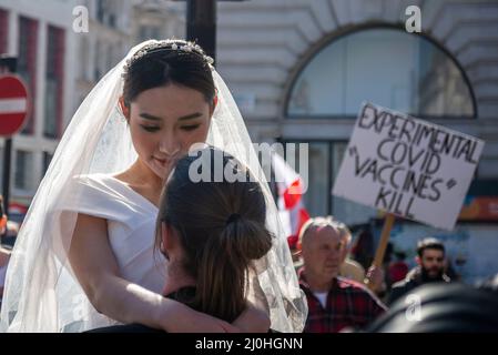 Westminster, London, Großbritannien. 19.. März 2022.Es Findet Ein Protest gegen die Impfung von Kindern für Covid 19 statt, dem auch Anti-Vaxxer beigetreten sind. Der marsch unterbrach ein Fotoshooting im Hochzeitskleid, wobei die asiatische Braut und der weiße Bräutigam trotzdem weitermachen. Covid-Plakat Stockfoto