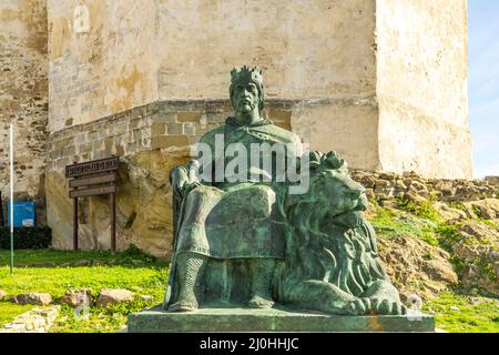 Das Denkmal für König Sancho IV El Bravo vor der Burg Guzman in Tarifa, Andalusien, Spanien | König Sancho IV El Bravo mit Löwendenkmal und dem c Stockfoto