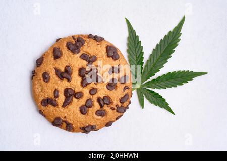 Amerikanische Cookies mit Cannabisextrakt. Süßigkeiten mit CBD-Öl. Marihuana Blätter auf weißem Hintergrund. Draufsicht, flach liegend. Stockfoto