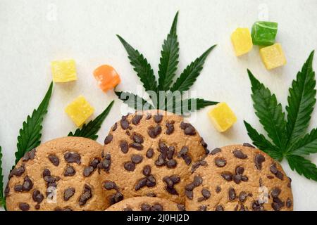 Amerikanische Cookies mit Cannabisextrakt. Süßigkeiten mit CBD-Öl. Marihuana Blätter auf weißem Hintergrund. Draufsicht, flach liegend. Stockfoto