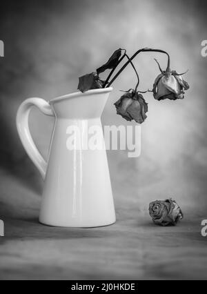 Trockene, welke Rosenblüten auf einer weißen Vase und Vintage Hintergrund Stockfoto