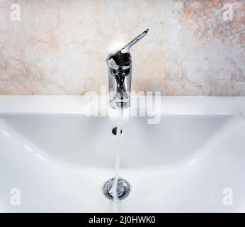 Verchromter Wasserhahn mit Hebel zum Mischen von heißem und kaltem Wasser auf einem modernen weißen Waschbecken in einem Badezimmer Stockfoto