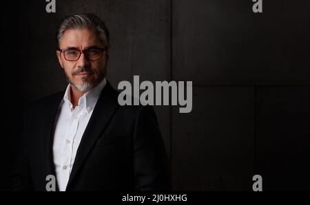 Geschäftsporträt eines älteren Mannes im Jahr 50s mit grauen Haaren vor dunklem Hintergrund. Geschäftsmann in Brille, kopieren Raum. Stockfoto