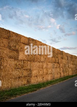 Heuballen stapelten sich auf einem Feld gegen den blauen Himmel mit Wolken Stockfoto