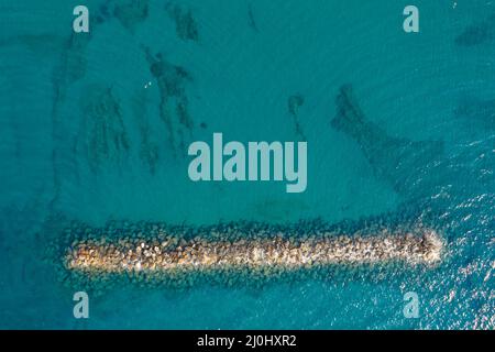 Luftaufnahme von einer fliegenden Drohne aus blauem Meerwasser und Wellenbrecher. Stockfoto