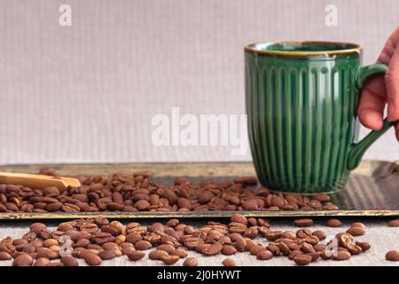 Hand nehmen Tasse Kaffee mit viel Kaffeebohnen und Holzlöffel auf Tablett aus nächster Nähe. Leerer Kopierbereich im Hintergrund. Stockfoto