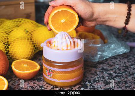 Frau drückt Orange mit Entsafter oder Quetschpresse auf dem Hintergrund der Küchenarbeitspresse. Kein Zucker- oder zuckerfreier, köstlicher Orangensaft-Zubereitungsvorgang Stockfoto