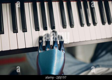 Im Musikgeschäft spielt ein junger behinderter Mann auf einem elektronischen Klaviersynthesizer mit künstlicher prothetischer Hand. Stockfoto