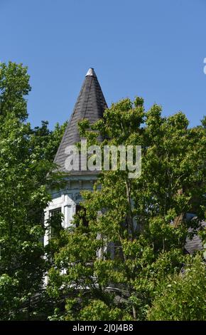 Altes, historisches, viktorianisches Haus wurde überwuchert und verlassen. Der runde Turm ist mit einer Zinnkappe und Schindeln gekrönt. Die Farbe ist rissig und blättert ab. Stockfoto