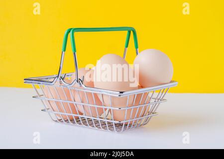 Hühnereier in einem Einkaufswagen. Eier im Laden. Frische Lebensmittel im Regal. Lebensmittelkorb. Nahaufnahme auf weißem Hintergrund, Draufsicht. Stockfoto
