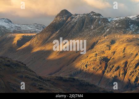 Dramatisches launisches Licht trifft an einem bewölkten Winternachmittag im rauen English Lake District auf die Seite der Bergkette. Langdale Pikes, Großbritannien. Stockfoto