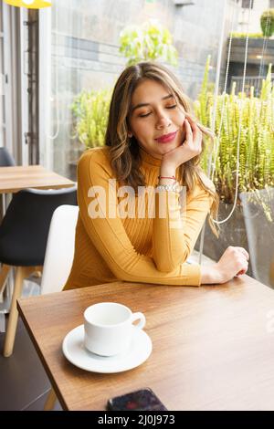 Morgen ruhen an einem Tisch sitzen eine schöne, junge, lateinische Frau mit blonden Haaren, Frühstück, heiße Getränke in einer Tasse, Schönheit und Lifestyle Stockfoto