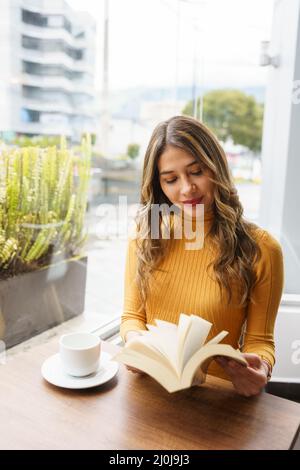 Entspannte junge latinerin mit langen blonden Haaren, genießen Sie eine Tasse heißes Getränk und lesen und lernen Sie aus einem Buch, Lifestyle und intellektuellen Hobby, Make-up Stockfoto