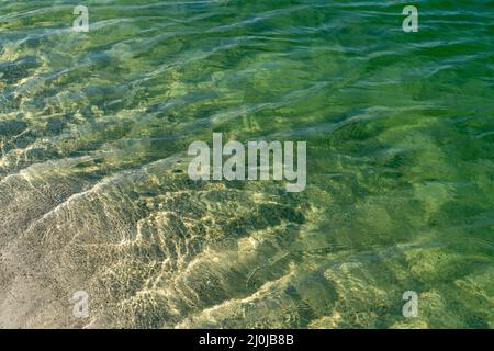 Hintergrund einer abstrakten Nahaufnahme von Wellen in klarem und flachem hellblauem Wasser mit Kalksteinsand darunter Stockfoto