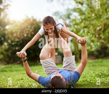 Wir haben den Weg frei. Aufnahme eines Vaters, der seine Tochter mit den Beinen hochhob, während er tagsüber auf dem Gras eines Parks lag. Stockfoto