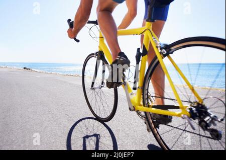 Genießen Sie die Landschaft beim Training. Beschnittene Ansicht eines Radfahrers, der entlang einer Meeresstraße radelt. Stockfoto