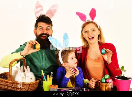 Glückliche Familie mit Ostern bunte Eier. Mutter, Vater und Sohn in Hasenohren sitzen am Holztisch. Stockfoto