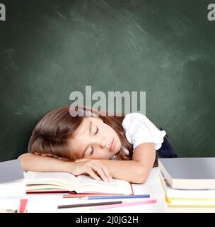 Ein müdes kleines Mädchen, das in der Schule auf dem Schreibtisch schläft. Stockfoto