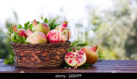 Reife und saftige Granatäpfel im Korb auf Holztisch. Ein voller Granatapfelkorb mit roten Früchten der Herbsternte Stockfoto