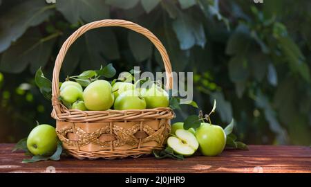 Grüne Äpfel im Korb auf einem Holztisch über dem Gartenhintergrund. Ernährung und gesunde Lebensweise Konzept. Horizontale Ansicht mit Kopierbereich Stockfoto