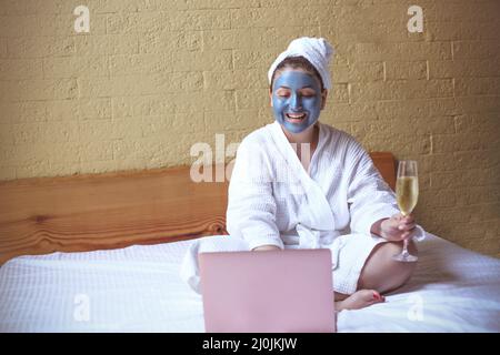 Junge Hipster-Frau lächelt, während sie Champagner während eines Videoanrufs über den Laptop zu Hause trinkt Stockfoto