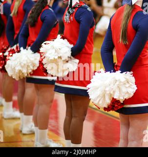 High School Cheerleader stehen vor der Tribüne mit ihren Pom Poms hinter ihnen whatching ihre Teams Basketball-Spiel. Stockfoto