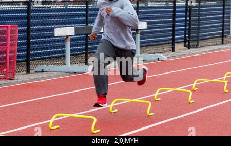 Ein Nachschulläufer läuft während des Trainings über kleine gelbe Mini-Hürden, die die Wicket-Sportübung ausführen. Stockfoto