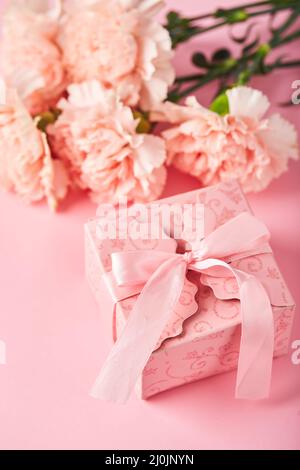 Bouquet von rosa Nelken und rosa Geschenkbox. Design Konzept der Feiertagsgrüße mit Nelkenstrauß auf rosa Hintergrund Stockfoto