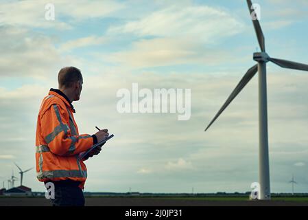 In der Gesellschaft von Riesen. Aufnahme eines jungen Ingenieurs, der eine Windenergieanlage inspiziert. Stockfoto