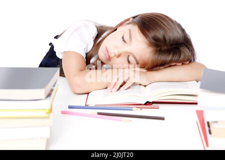 Ein müdes kleines Mädchen, das in der Schule auf dem Schreibtisch schläft. Stockfoto