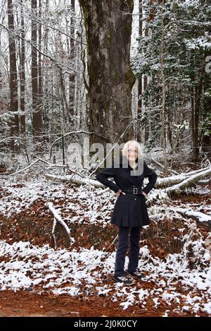 Eine ältere Frau, 100 Jahre alt, steht mit den Händen auf den Hüften. Sie genießt einen Spaziergang, im Süden von Arkansas, durch einen verschneiten Wald. Stockfoto