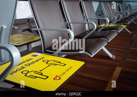 Gelbes soziales Distanzschild auf den Liegestühlen am Flughafen. Sicherheitsmaßnahmen nach der Pandemie Covid-19 Stockfoto