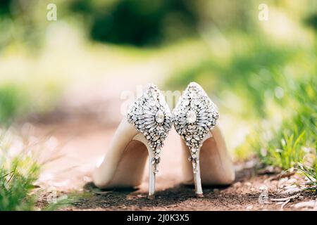 Schuhe der Braut mit einem Hintergrund mit Steinen auf dem Boden in der Natur mit geringer Tiefe des Feldes verziert. Stockfoto