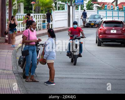 San Andrés, San Andrés y Providencia, Kolumbien - November 17 2021: Schwarzer Mann mit Gesichtsmaske auf einem Motorrad kommt an zwei Frauen vorbei, die sich unterhalten Stockfoto