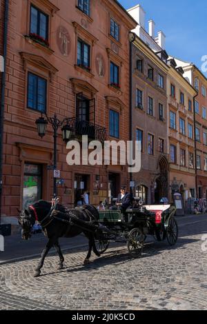 Schwarzes Pferd und Kutsche auf einer Kopfsteinpflasterstraße in der historischen Altstadt von Warschau Stockfoto