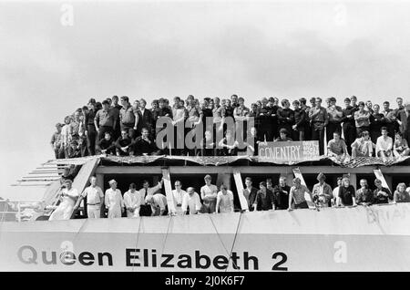 QE2 kehrt nach Southampton zurück. Union Jacks sind auf Autos festooniert, auf Schultern drapiert, auf Stöcken gewellt. Southampton begrüßt den Luxusliner aus dem Jahr QE2, der zum Trooper wurde und aus dem Krieg zurückkehrt, mit einem „Three Cheers“. An Bord ist ihre kostbare Fracht, die 700 Überlebenden der HMS Coventry, Ardent und Antelope, im Kampf um die Falklands versunken. 11.. Juni 1982. Stockfoto