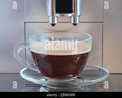 Eine Kaffeemaschine bereitete eine Tasse Kaffee in der Glastasse und einer Untertasse zu Stockfoto