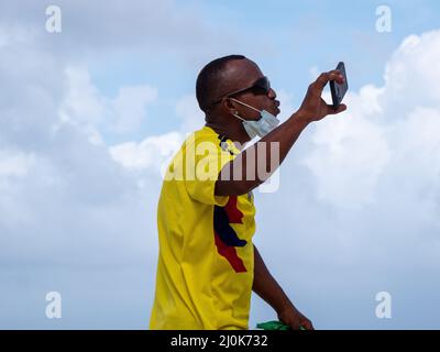 San Andrés, San Andrés y Providencia, Kolumbien - November 17 2021: Schwarzer Mann mit Sonnenbrille und Maske hält sein Handy und seine Filme am Strand Stockfoto