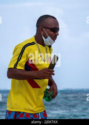 San Andrés, San Andrés y Providencia, Kolumbien - November 17 2021: Schwarzer Mann mit Sonnenbrille und Maske hält sein Handy und seine Filme am Strand Stockfoto